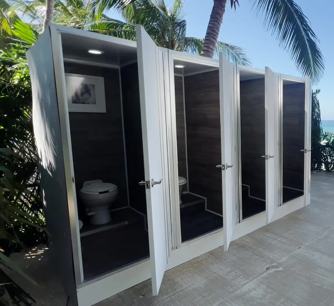 Interior de unidades de baños portátiles VIP de lujo con acabados en madera, iluminación LED, inodoros premium y vista al mar con palmeras — Luvory